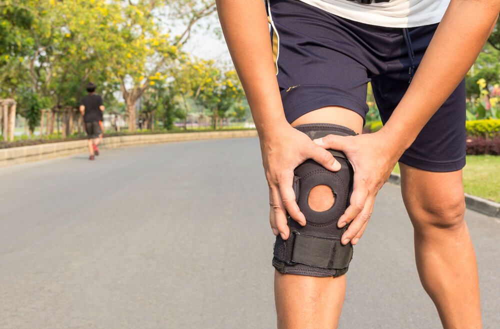 Man Adjusts Knee Brace During Run in Park